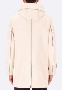 Cappotto di velluto a coste beige con un grande colletto strutturato e dettagli sulle cuciture laterali. Presenta coste verticali e una silhouette dritta.