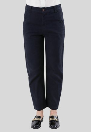 Donna che indossa pantaloni blu navy a gamba dritta con tasche frontali e mocassini neri in vernice con fibbie dorate.