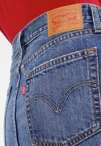 Jeans av medelblå denim med en läderetikett, röd flik och förstärkta sömmar på bakfickorna i en klassisk design.