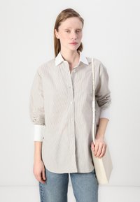 Gestreept overhemd in lichtbeige en wit, met een contrasterende witte kraag en opgerolde mouwen; gecombineerd met een minimalistische beige tas.