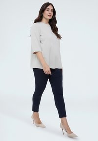 Lichtgrijs topje met korte mouwen en een bloemrijke textuur, gecombineerd met marineblauwe nauwsluitende broek en naaktkleurige pumps met spitse neus, wat zorgt voor een gestroomlijnd silhouet.