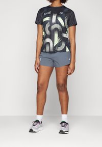 Person wearing a black graphic athletic t-shirt, gray running shorts, white socks, and gray running shoes with pink and green accents.