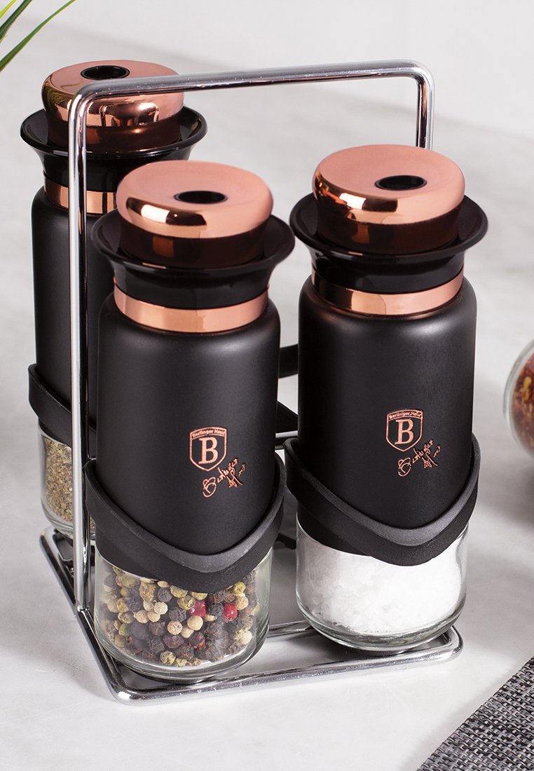 Set aus drei Gewürzbehältern mit mattschwarzen Außenflächen und Kupferdeckeln, die bunte Gewürze und Salz enthalten, montiert in einem Metallregal.