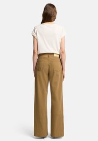 T-shirt a maniche corte color beige chiaro abbinato a pantaloni beige a vita alta con gamba larga, caratterizzati da una superficie liscia e due tasche posteriori.