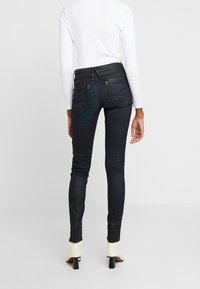 Tajta jeans i mörk tvätt, med en slät yta, bakfickor och läderliv, kombinerat med en figurnära vit topp.