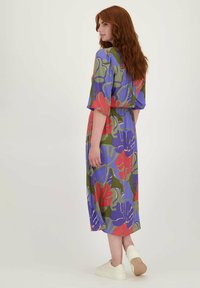 Bloemenprint jurk in blauw, groen, rood en paars. Heeft korte mouwen, een tailleband en een midi-lengte. Gecombineerd met witte sneakers.