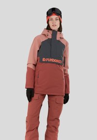 Kurtka narciarska w kolorach różowym, szarym i czerwonym, z wysokim kołnierzem, logo na wysokości talii oraz pasującymi spodniami. W zestawie rękawice i czapka.