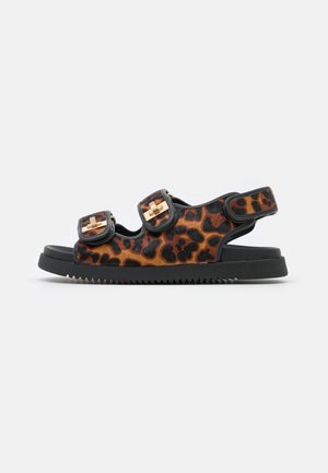Offener Zeh-Sandalette mit braun-schwarzem Leopardenmuster, zwei Klettverschlüssen mit goldenen Schnallen und einer schwarzen Sohle mit geriffeltem Profil.