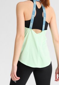 Sportowy top Nike w miętowym kolorze z czarnymi ramiączkami. Posiada design typu racerback, miękką teksturę i otwarty krój z tyłu.