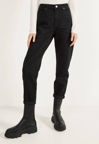 Jeans negros de cintura alta con puños enrollados, hechos de mezclilla. Combinados con botas negras de cuero grueso con suelas texturizadas.