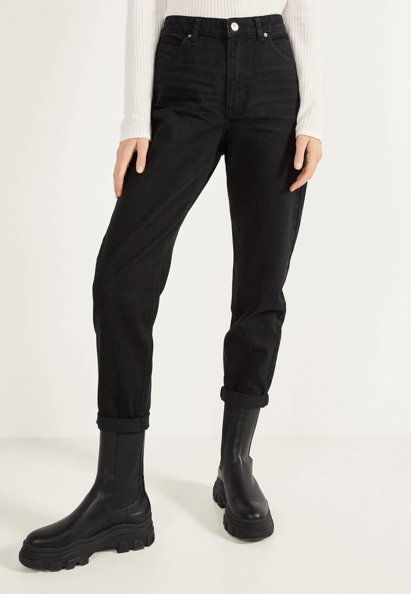 Jeans negros de cintura alta con puños enrollados, hechos de mezclilla. Combinados con botas negras de cuero grueso con suelas texturizadas.