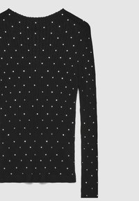 Maglione nero lavorato a maglia con maniche lunghe, caratterizzato da una texture a coste e da decorazioni metalliche sparse su tutta la superficie. Scollo rotondo.