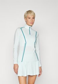 Light blue long-sleeve athletic top with a high collar, featuring teal side accents and a half-zip closure, paired with a pleated skirt.