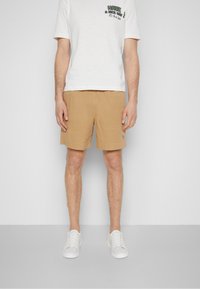 Pantalones cortos beige hechos de un tejido suave, con un corte recto y dobladillos enrollados. Combinados con una camiseta blanca y zapatillas blancas.