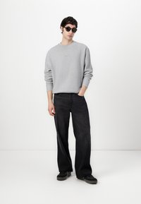 Gray crew-neck sweatshirt with ribbed cuffs, paired with dark, wide-leg jeans and black sneakers, complemented by black sunglasses.