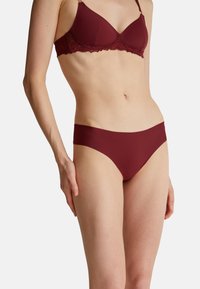 Burgunderfarbens Lingerie-Set mit einem gepolsterten BH mit Spitzenbesatz und nahtlosen Bikiniunterteilen in einer glatten Textur und minimalistischem Design.