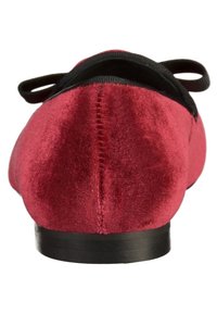 Rote Velours-Ballettschuhe mit einer schwarzen Stoffschleife vorne, flache schwarze Sohle und sichtbaren Nähten entlang der Rücknaht.