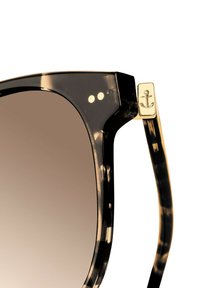 Zonnebril met een donker schildpadframe, voorzien van een gouden ankeraccent op de poot en gradient bruine lenzen.