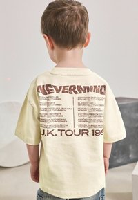 T-shirt en coton jaune clair avec un grand motif marron au dos, listant les dates et lieux de la "TOURNEE AU ROYAUME-UNI 1993."