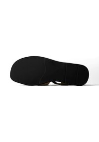 Semelle de chaussure noire avec zone texturée à l'avant et talon lisse, reposant sur une surface blanche vue de dessous.