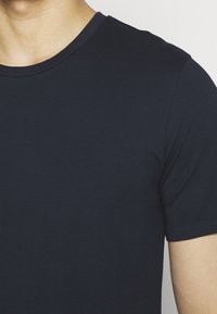 Námořnické modré tričko s krátkým rukávem vyrobené z hladkého, lehkého materiálu. Má kulatý výstřih a minimální švy na lemu.