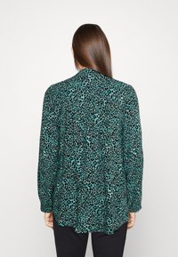 Långärmad blus i turkos med ett mönster av svart djurprint. Har rund halsringning och avslappnad passform, tillverkad av lätt material.