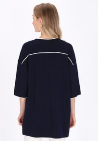 Maglietta oversize blu navy con maniche a 3/4. Piping bianco a contrasto lungo le spalle e le maniche. Tessuto morbido, vestibilità rilassata, orlo arrotondato.