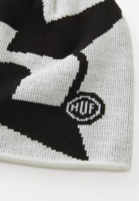 Zwart-witte gebreide stof met gedurfde geometrische patronen en een klein rond logo met de letters "MUC".