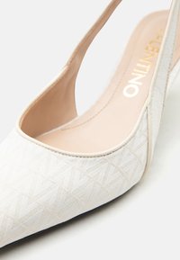 Λευκό παπούτσι με μύτη σε μυτερή μύτη, υφή γεωμετρικού μοτίβου και μπεζ εσωτερική επένδυση.