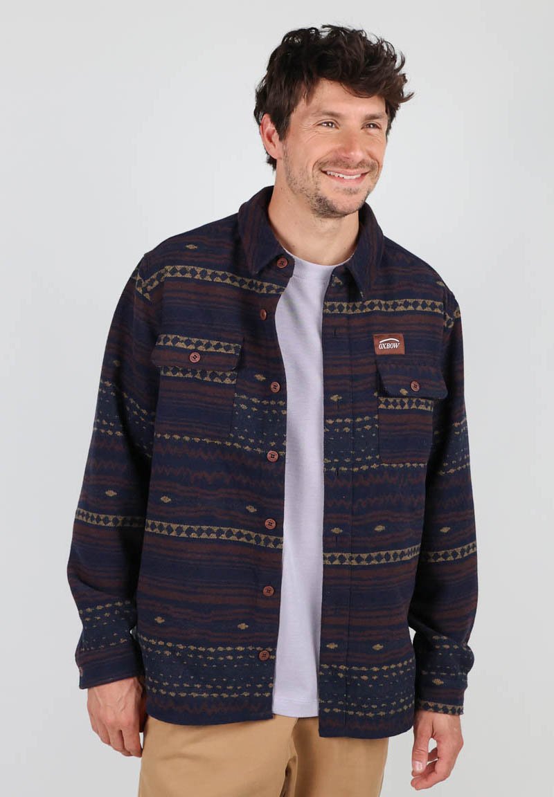 Chemise en flanelle à motifs navy avec des designs géométriques en marron et vert, dotée d'une fermeture boutonnée à l'avant et de poches sur la poitrine.