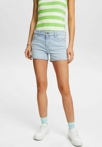 Bermudas de mezclilla azul claro con un diseño ajustado, que cuentan con un cierre frontal de botón, bolsillos traseros y un dobladillo enrollado. Combinadas con una blusa de rayas verde y blanca.
