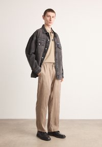 Veste en denim noir, polo beige, pantalon ample beige, chaussures noires. Textures lisses, design décontracté, poches proéminentes et détails de cordon de serrage.
