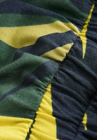 Gros plan d'un tissu froncé avec des rayures vertes, jaunes et bleu foncé montrant la texture et les détails de couture.