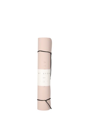 Donna con capelli ricci che tiene un tappetino da yoga arrotolato con tracolla sulla spalla, indossa un top scuro senza maniche e leggings neri su sfondo bianco.
