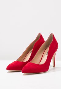 Röda mocka högklackade pumps med spetsig tå och slät innerfoder, som har en smal stilettklack och minimalistisk design.
