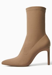 Vaaleanruskea nilkkuri, jossa on kärjestä teräväkärkinen ja tiukasti istuva sileä yläosa sekä korkea piikkikorko. Yläreunassa on tikkauskoristelu. Ei näkyvää metalliosaa.