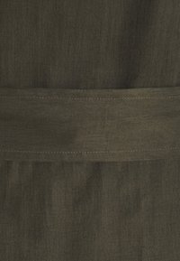 Tessuto verde oliva scuro, texture liscia e lucentezza sottile. Presenta una fascia orizzontale con dettagli di cucitura a contrasto.