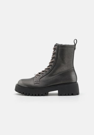 Bottine chelsea en cuir gris avec une semelle noire épaisse, un laçage à l'avant et une languette à l'arrière. Texture lisse et design durable.