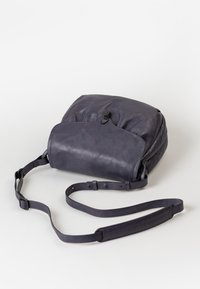 Borsa a tracolla in pelle viola con forma arrotondata, chiusura con zip, tracolla regolabile e superficie liscia. Design minimalista con dettaglio a pattina.