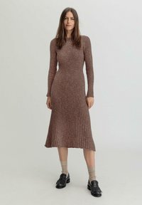 Gestreiftes, langärmliges Kleid in gedämpftem Braun, das bis zur Mitte der Waden reicht. Weicher Stoff, figurbetonte Silhouette mit einem weit schwingenden Saum. Kombiniert mit schwarzen Loafers und beigen Socken.