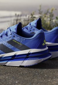 Blue athletic shoes featuring a textured mesh upper, black and neon green accents, and a layered, lightweight midsole for cushioning.