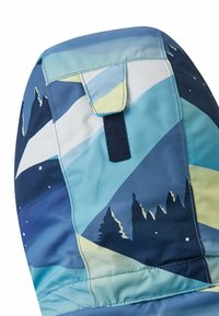 Zbliżenie niebieskiego materiału w wzory z sylwetkami gór i drzew, ukazujące mały klapek z ciemną prostokątną zakładką.