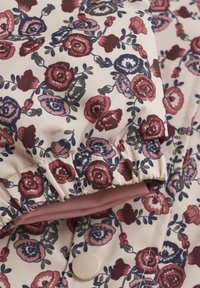 Blommig pufferjacka med krämfärgad bakgrund, prydd med röda och marinblå blommor. Samlade ärmslut och en rosa foder, stängd med en tryckknapp.