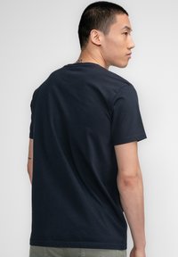 Camiseta de algodón azul marino con mangas cortas, cuello redondo y una textura suave, mostrada desde la parte de atrás.