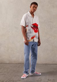 Chemise à manches courtes avec une base blanche, ornée d'un graphique audacieux de lèvres rouges. Associée à un jean bleu clair à jambes droites et des baskets blanches à motifs.