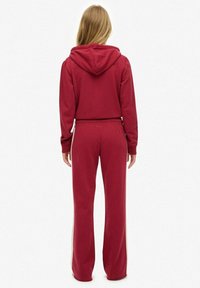 Maroon tracksuit set featuring a hooded sweatshirt and pants with side stripes. Made of soft fabric with a relaxed fit, simple design.