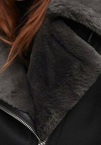 Veste en cuir noir avec une doublure et un col en fausse fourrure grise douce, fermeture éclair, et un design épuré avec une finition texturée.