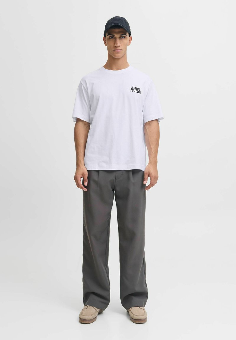 Hvid bomulds T-shirt med sort logo, parret med løstsiddende grå bukser. Lette beige mokkasinstil sko. Enkel design, ingen mønstre.