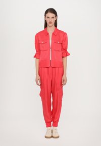 Felroze satijnen cropped jacket met pofmouwen en twee voorkruiken, gecombineerd met bijpassende broek met zijzakken en geribde boorden.