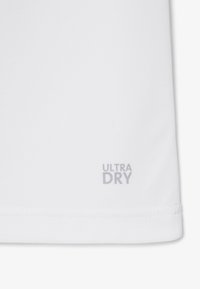 Weißer Stoff mit strukturierter Oberfläche und kleinem grauem Schriftzug "ULTRA DRY" nahe dem Saumrand gedruckt.